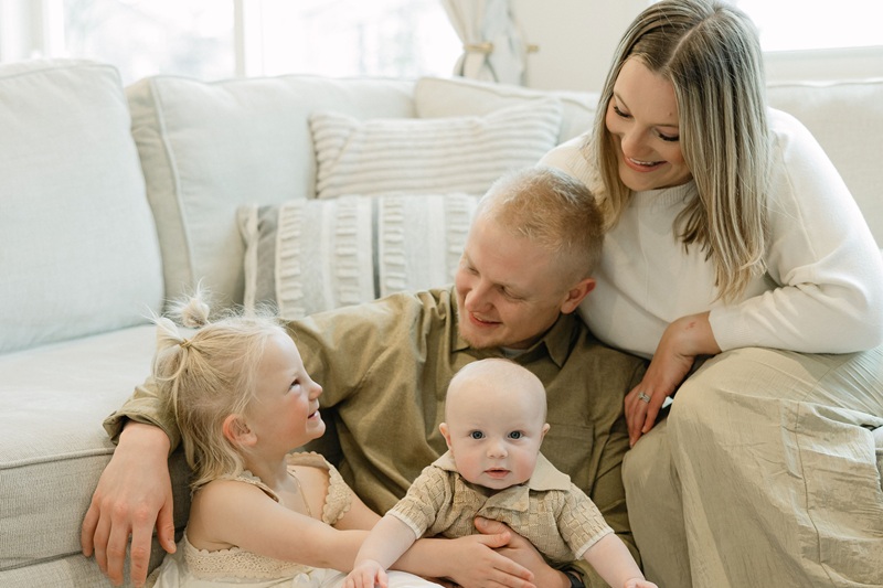 Family of four sitting on the couch and floor smiling together